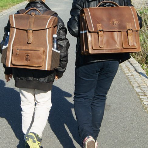 Ledertaschen by Freiherr von Maltzahn Zwei Kinder gehen mit braunen Rucksäcken aus Leder auf einem Weg.
