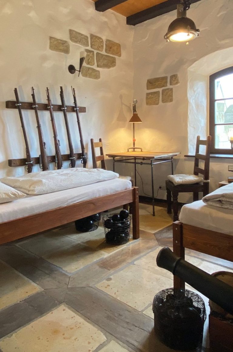 Waffenkammer im Rittergut Leppersdorf bei Radeberg Ein rustikales Zimmer mit Holzbetten, einem Tisch und Stühlen, Steinwänden und warmes Licht.